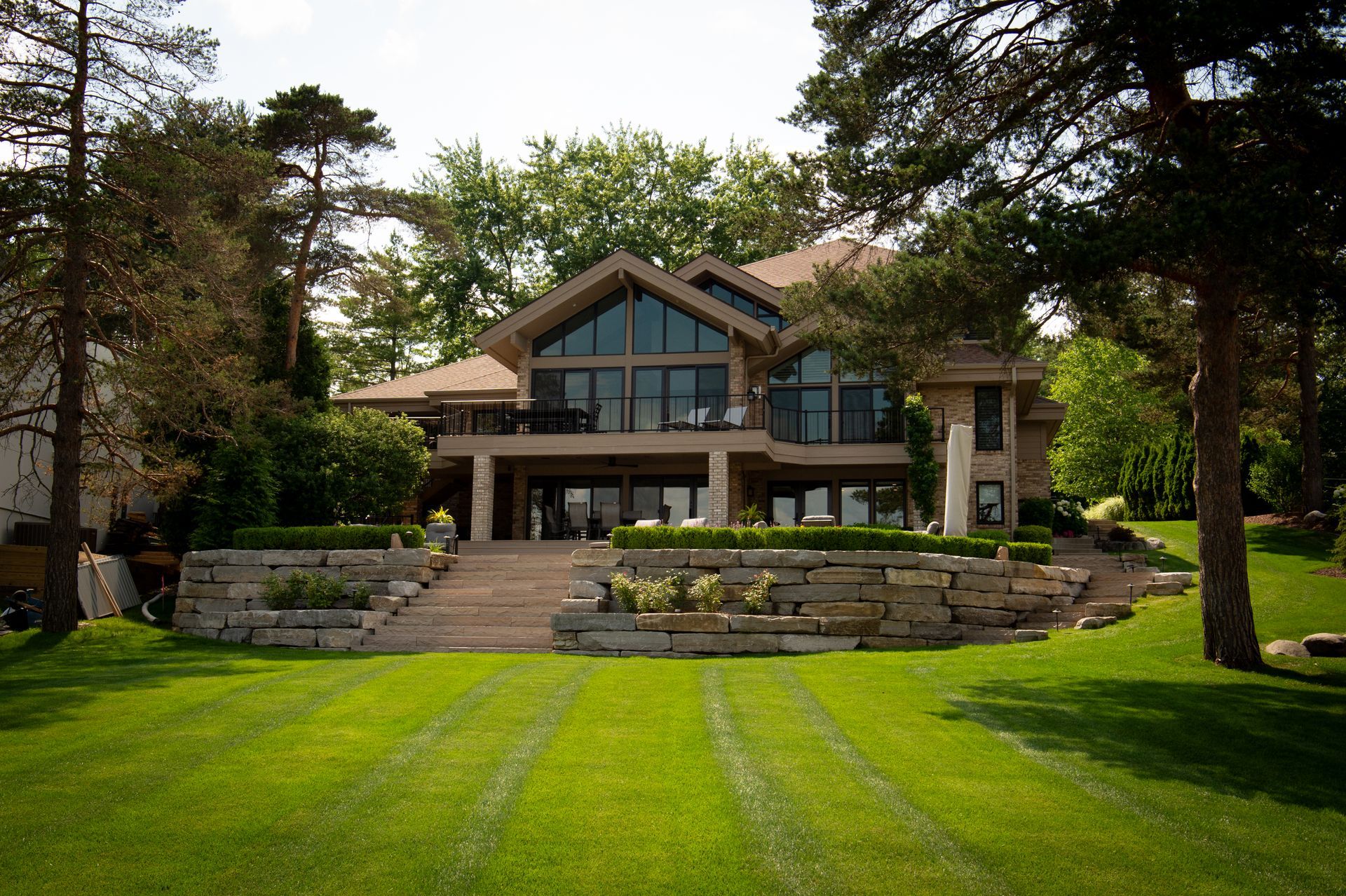 Luxury lakeside home with large windows, stone walls, and manicured lawn.