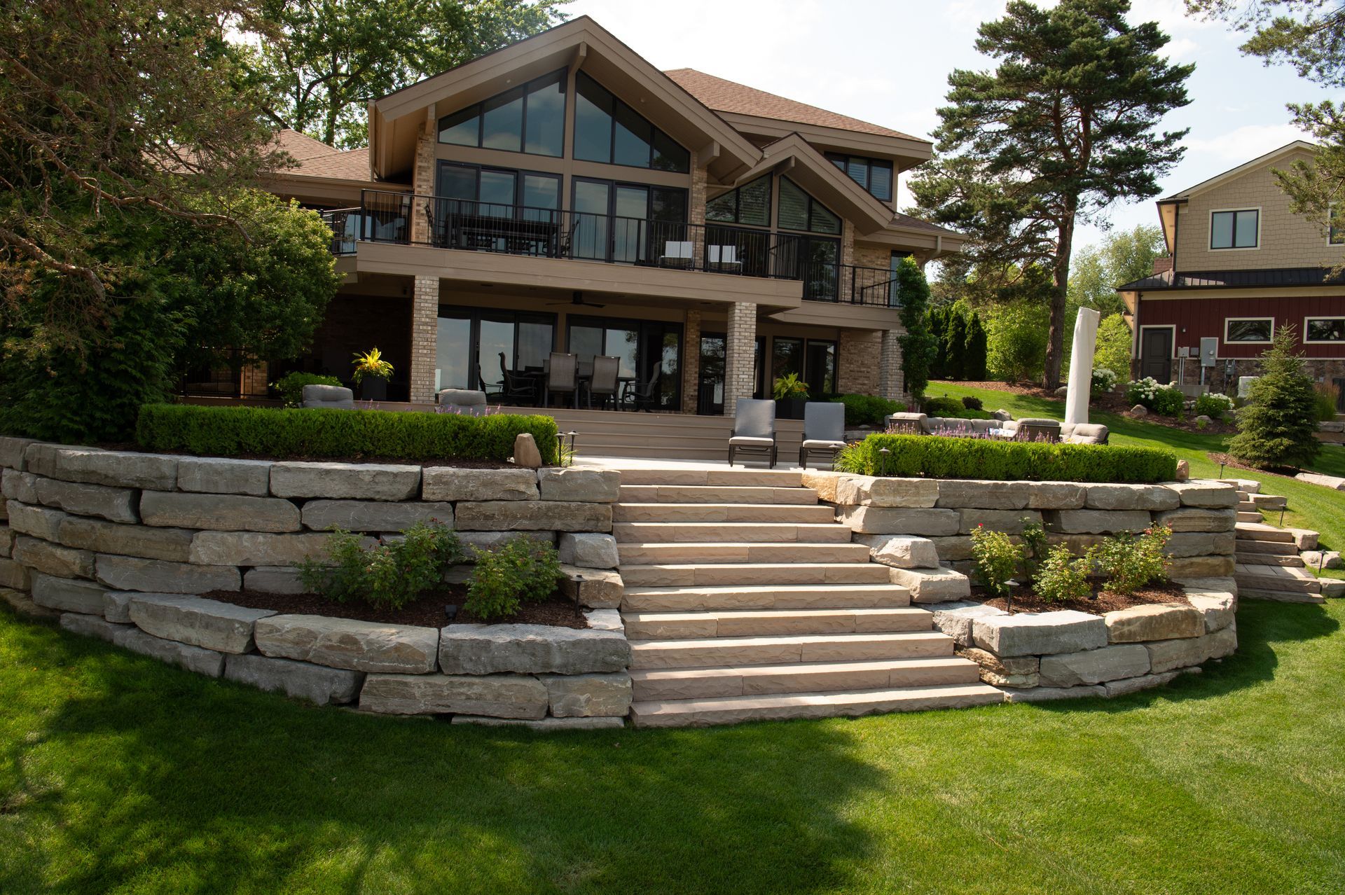 Two-story house with stone walls, steps, and large windows overlooking a lawn.