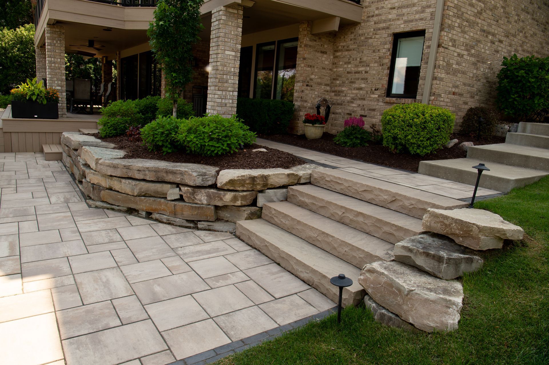 Stone steps and walkway lead to a brick house with landscaping and retaining wall.