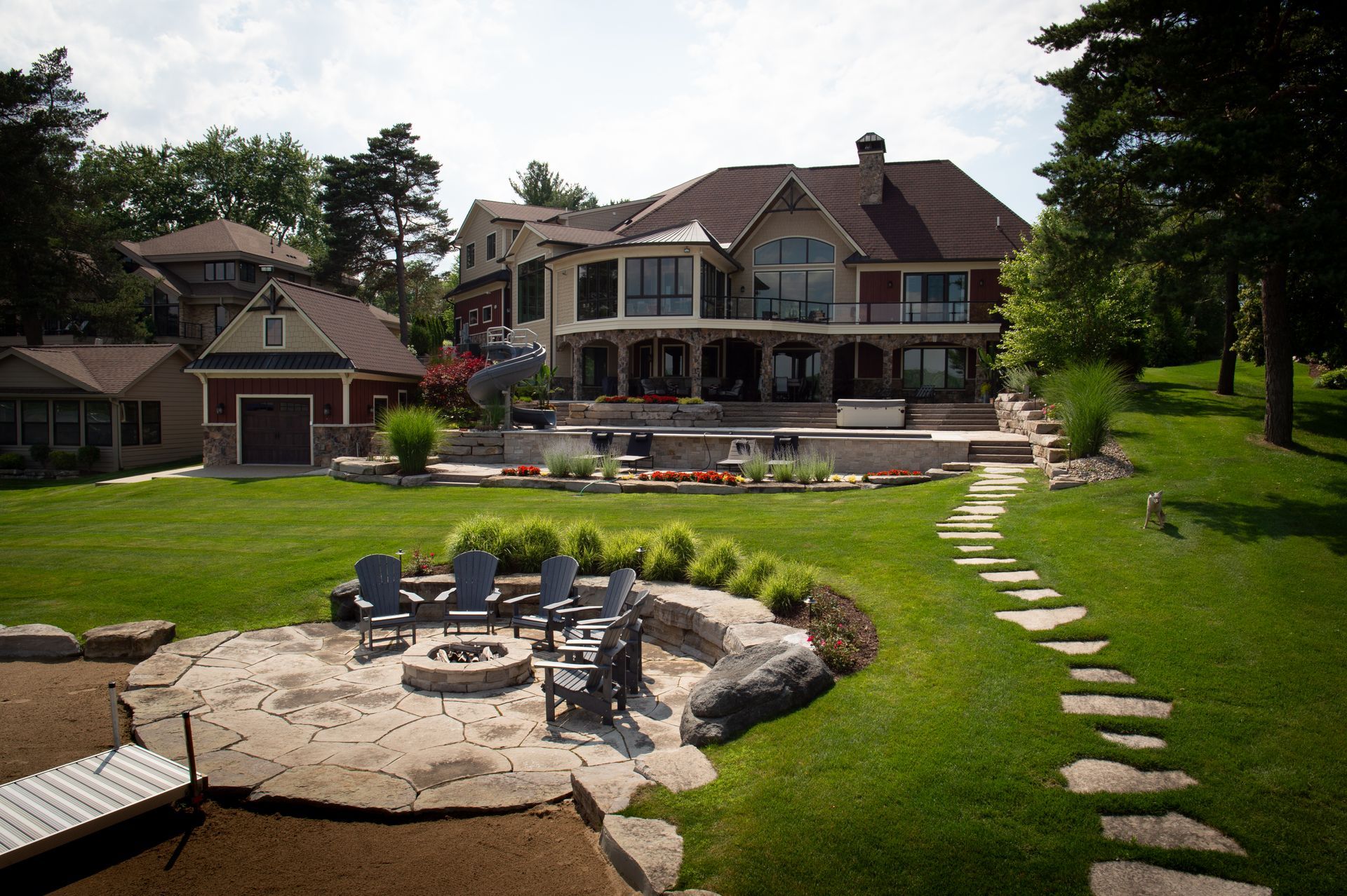 Large house with a fire pit area, lawn, and lake access.