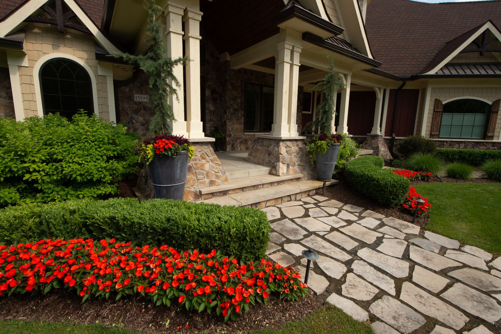 Stone pathway leads to a house with a porch and colorful landscaping.