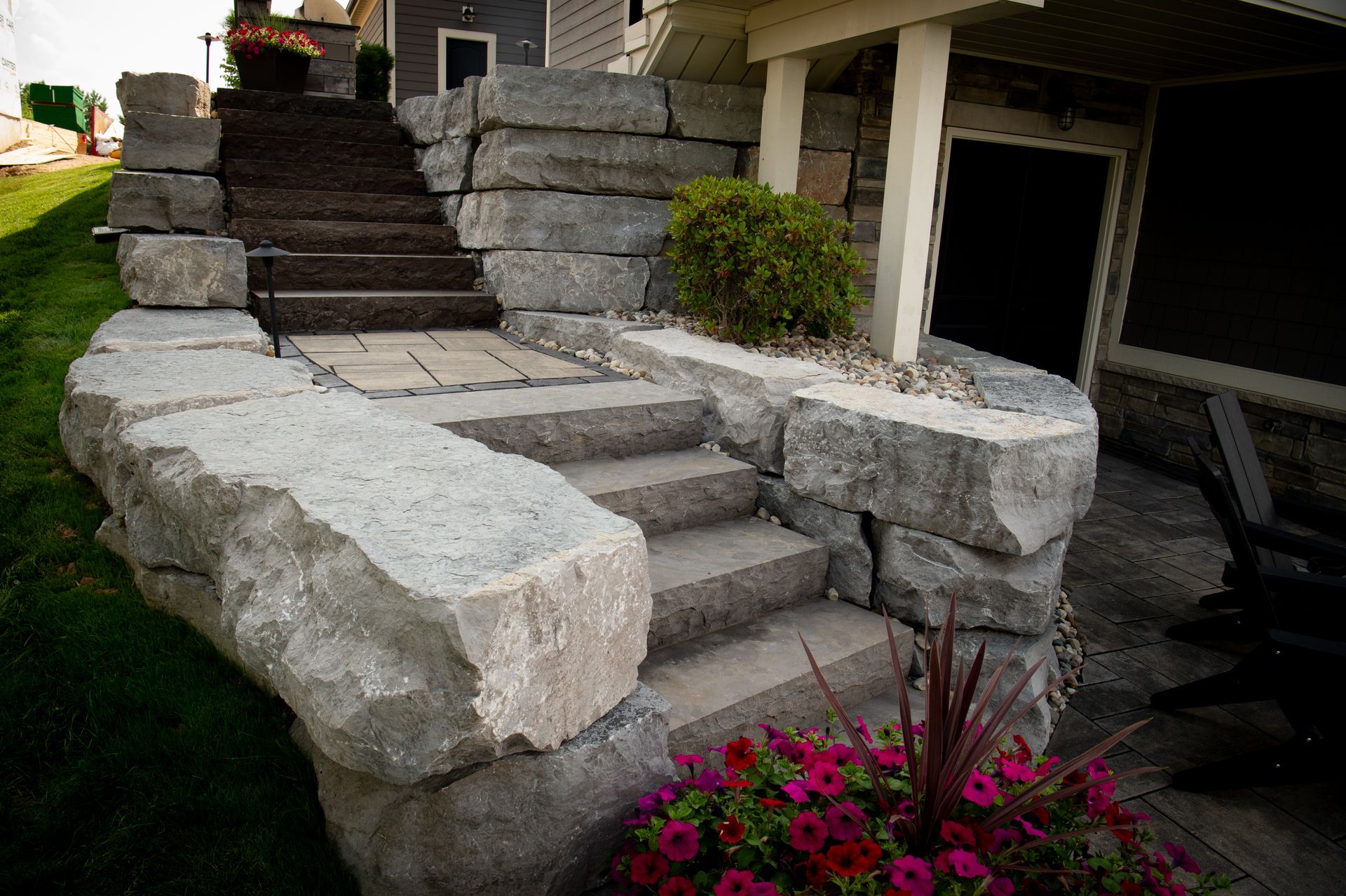 Stone staircase with retaining walls, leading to a home entrance, with plants and landscaping.