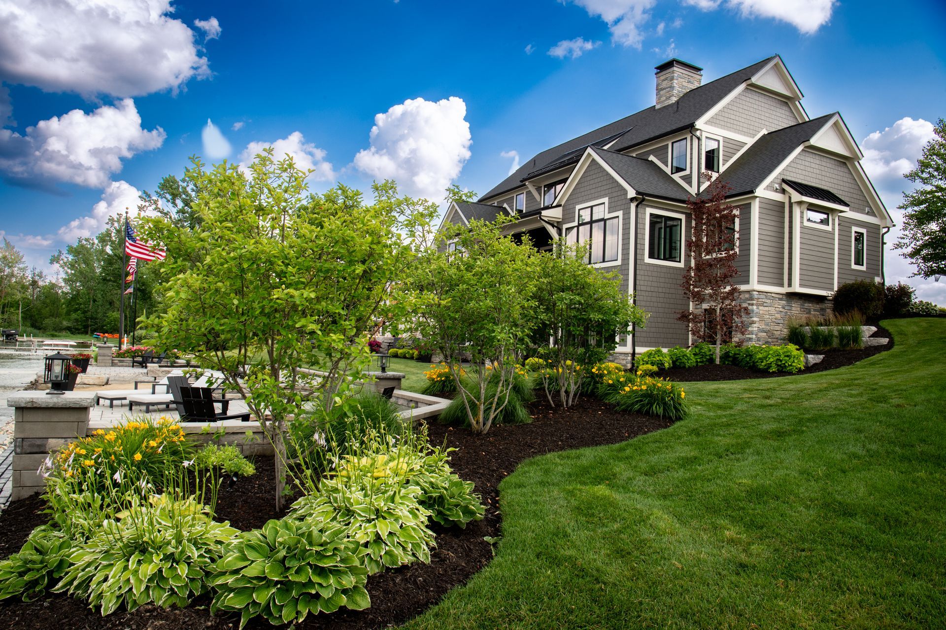 House with a gray exterior, lush landscaping, and blue sky with clouds.