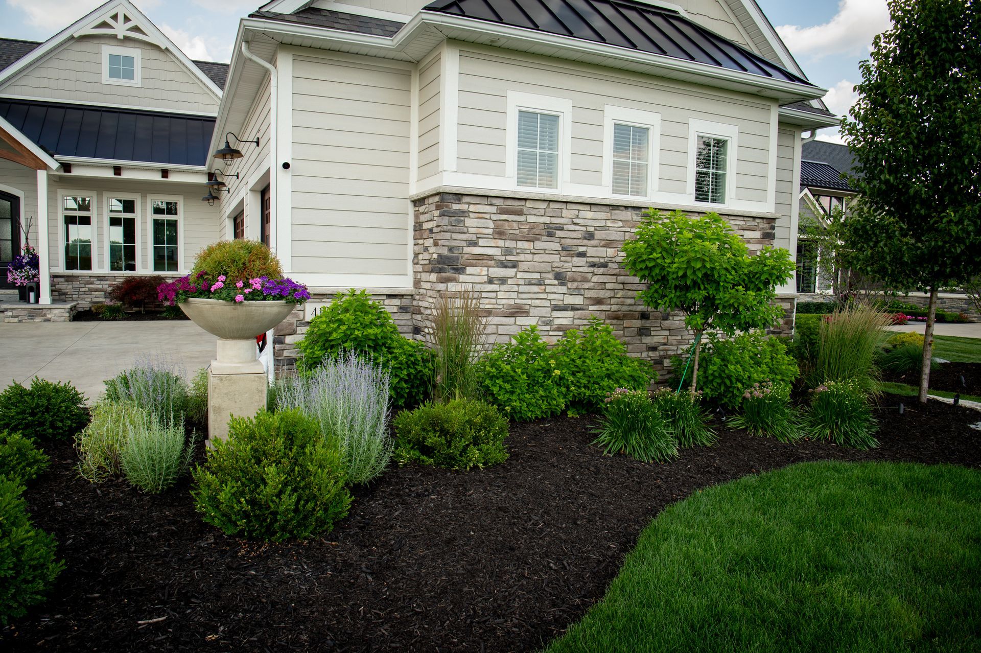 Landscaped front yard with a beige house, stone accents, and dark mulch.