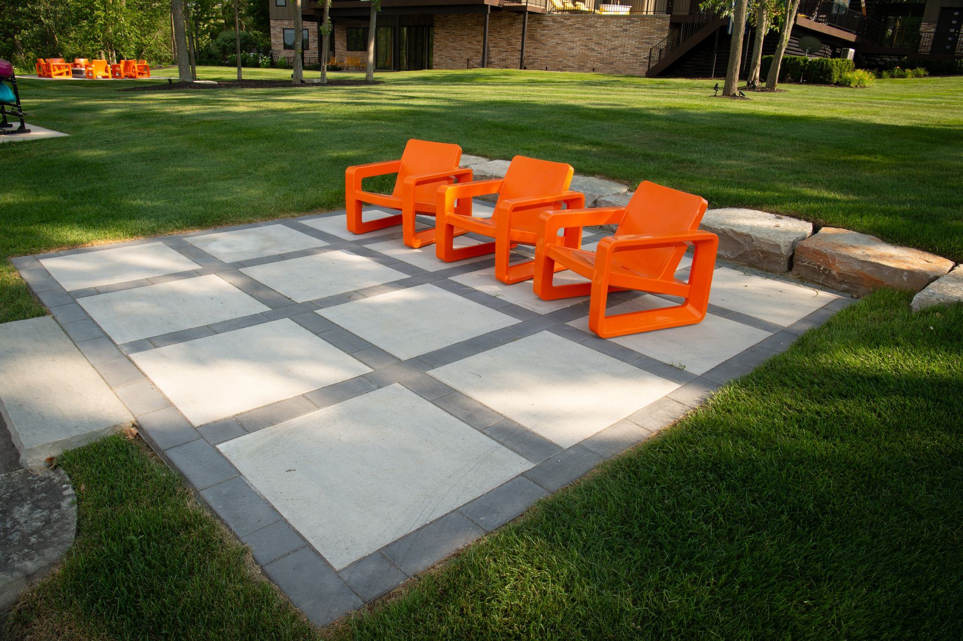 Four orange chairs on a gray and white patio, surrounded by grass.