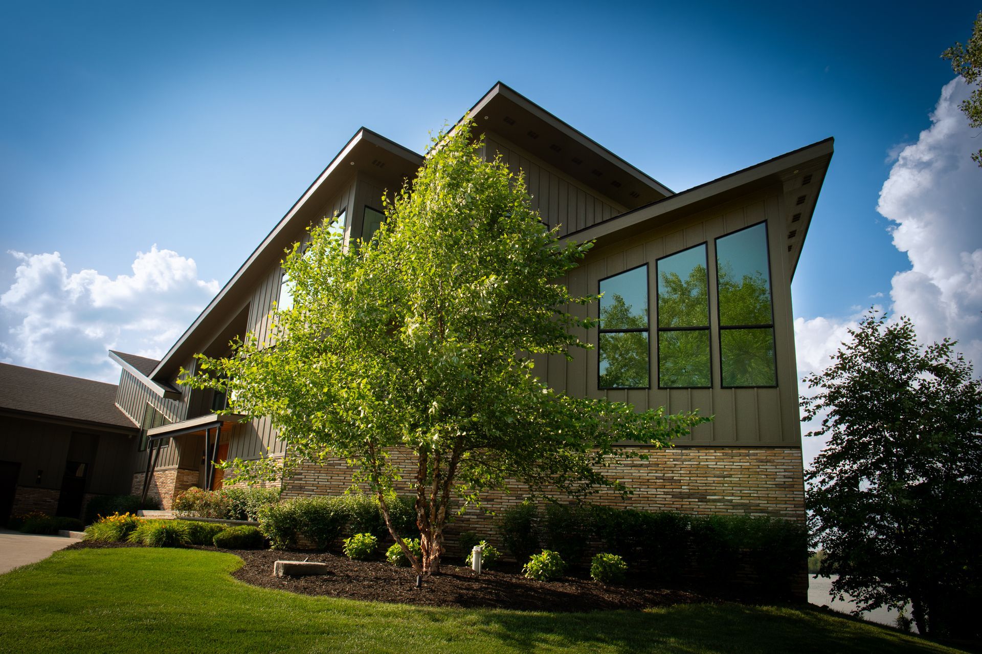 Modern building with a sloping roof, stone and wood siding, and large windows on a sunny day.