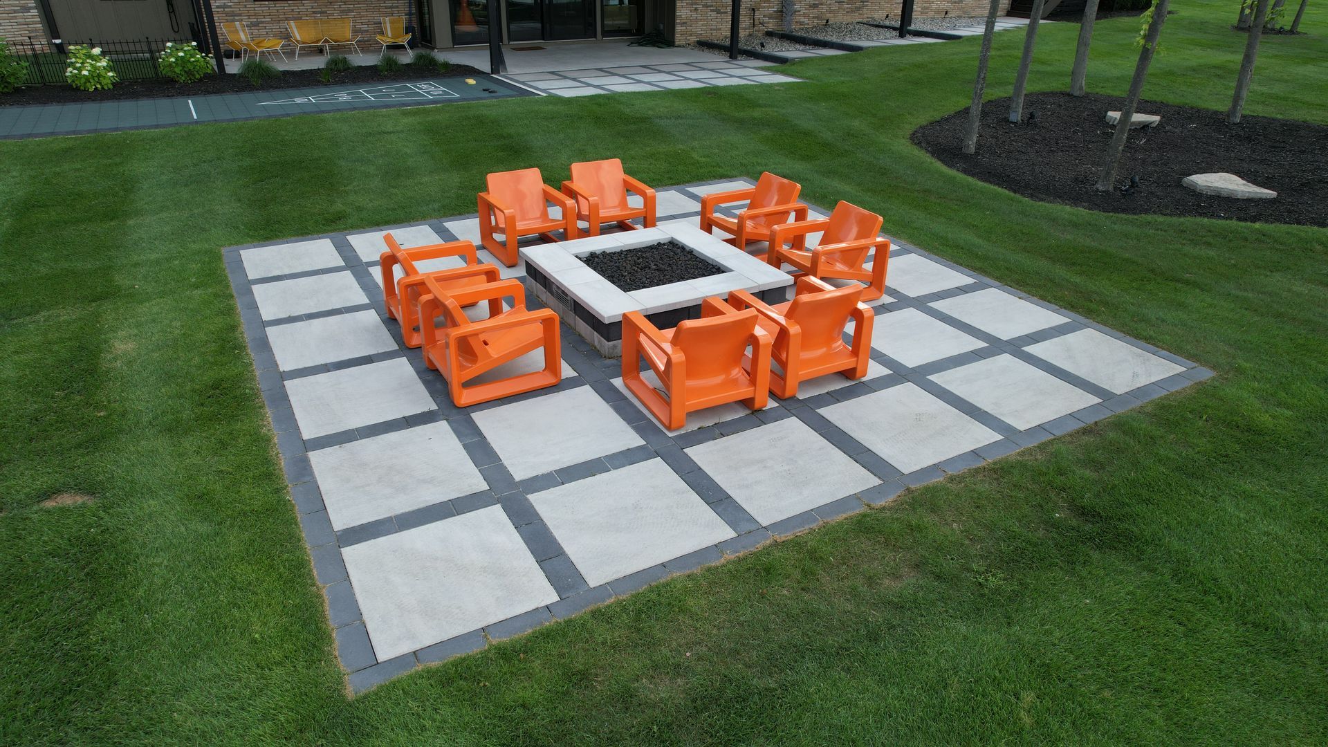 Orange chairs around a fire pit on a patio, surrounded by green grass.