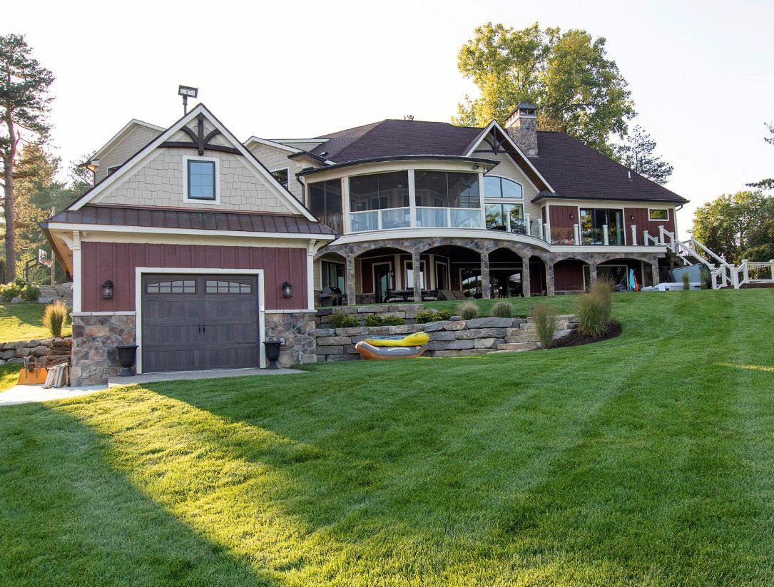 Large, multi-story house with red siding, stone accents, and a garage on a green lawn.