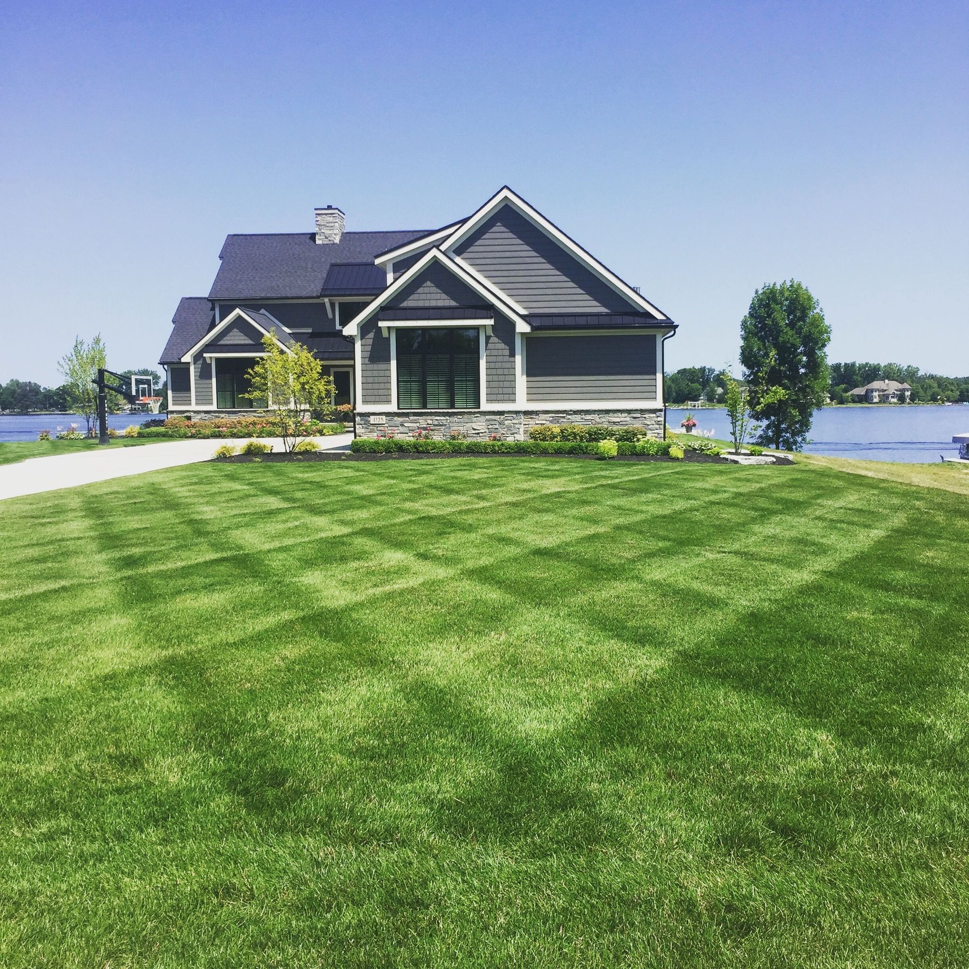 House with patterned lawn by water under blue sky.