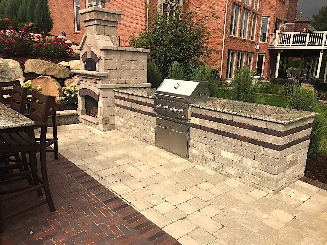 Outdoor kitchen with brick oven, grill, and countertop on a patio.
