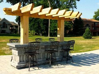 Outdoor bar with a stone base, wooden pergola, and bar stools on a patio.