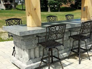 Outdoor stone bar with metal stools, next to a grassy lawn.