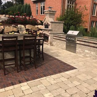 Outdoor kitchen with brick, stone, and a grill. Bar with stools and a pizza oven.