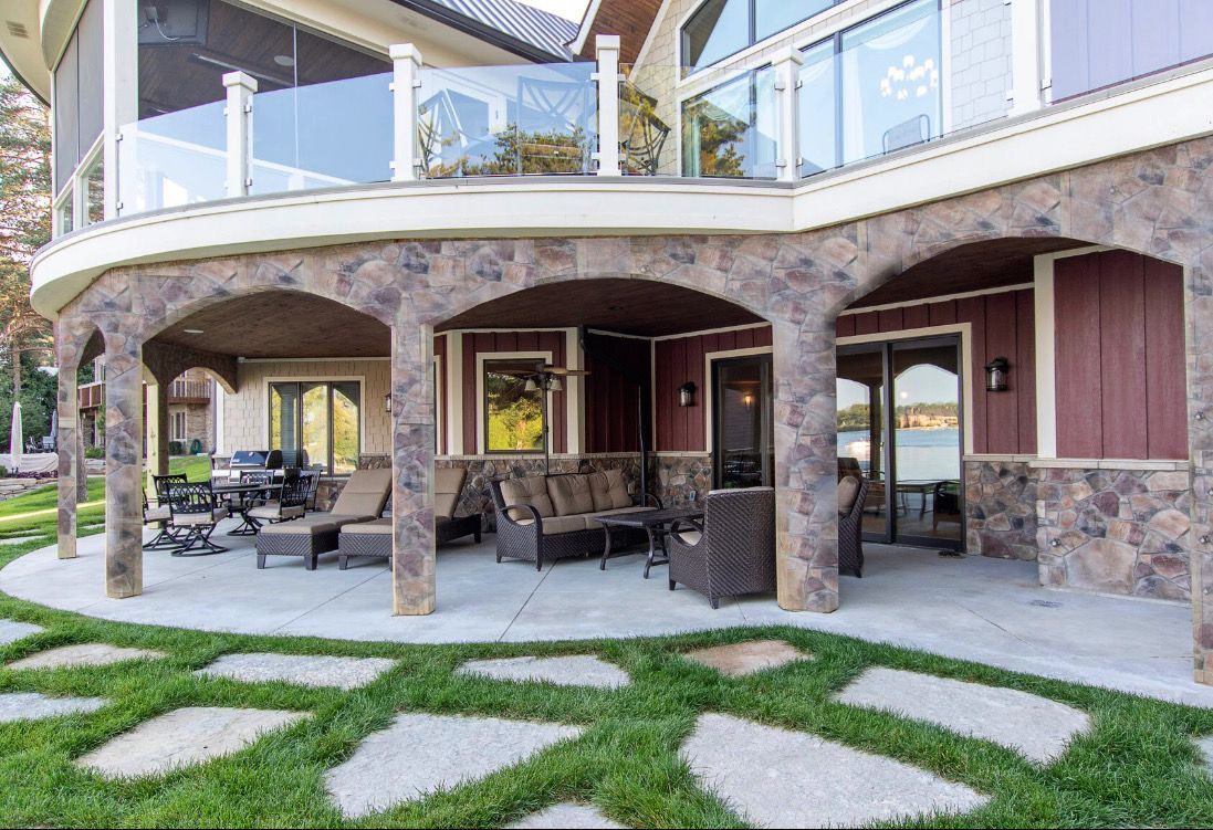 Stone patio with outdoor furniture, beneath a house with glass balconies.