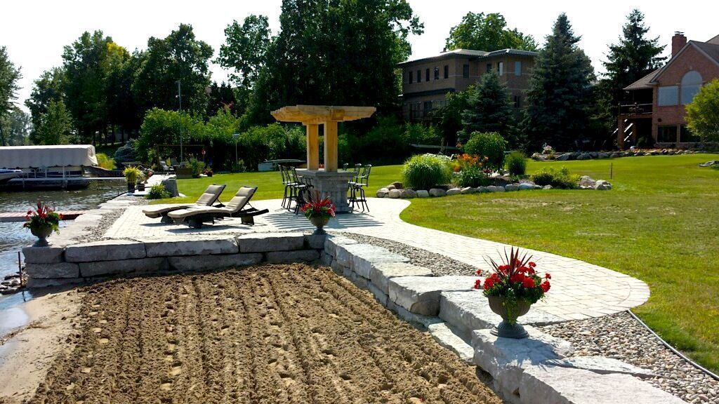 Stone patio with lounge chairs, path, gazebo, and waterfront view of a large lawn and trees.