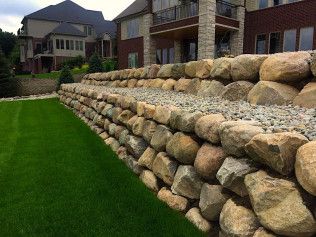 Large stone retaining wall bordering a grassy lawn, with a multi-story house in the background.