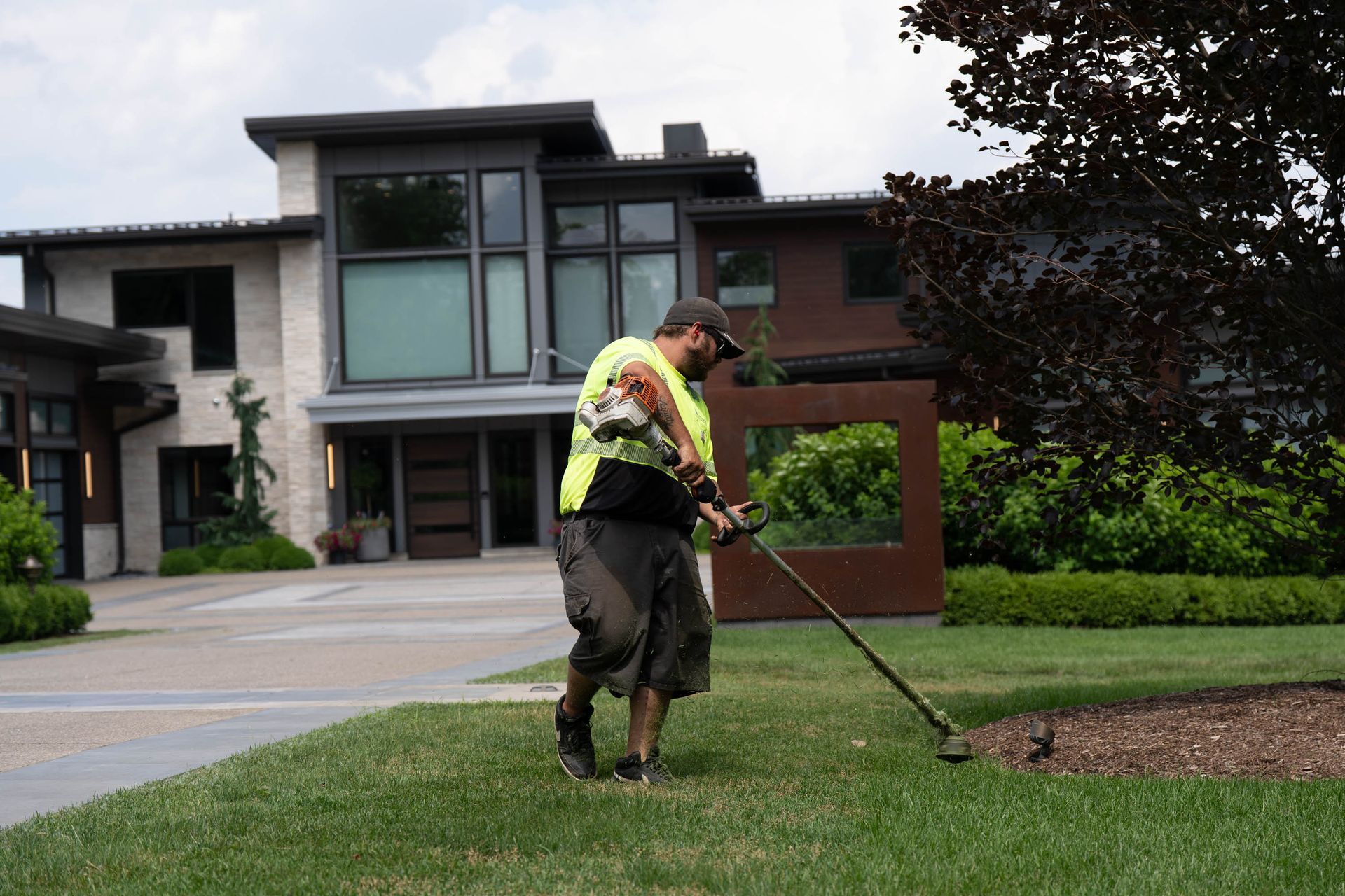 Man edging lawn with a trimmer in front of a modern house.