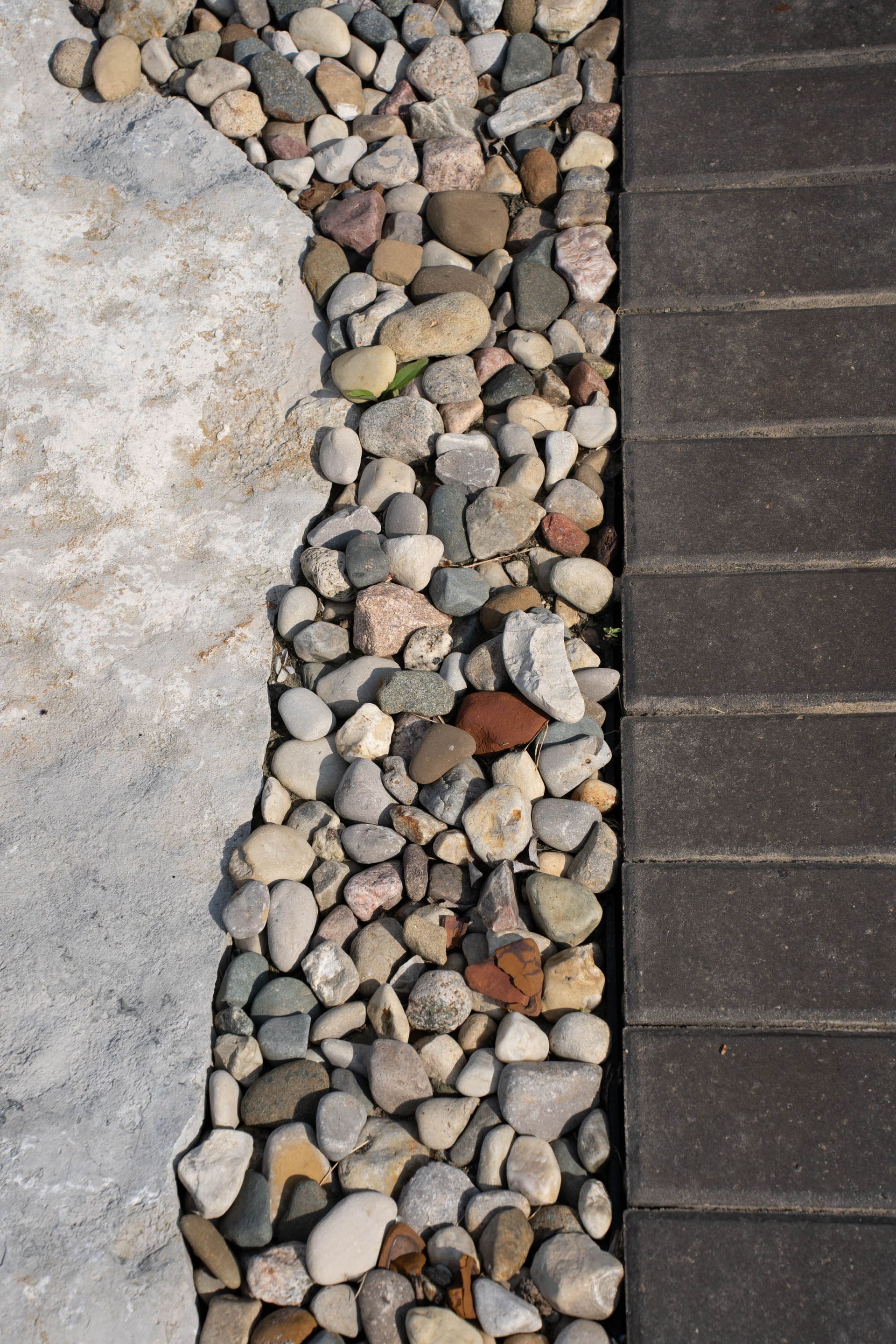 Gray stone pathway bordered by river rocks and dark brick pavers.