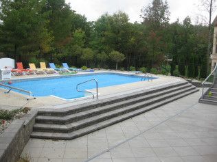 A rectangular pool with concrete steps and lounge chairs; trees in the background.