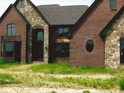 Brick and stone house with dark roof and oval window.