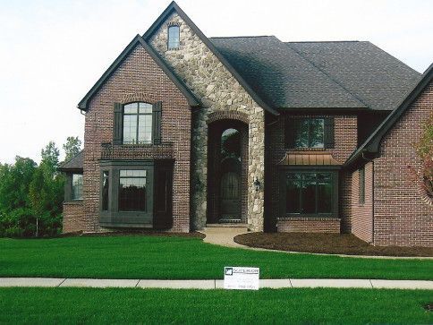 Two-story brick house with stone accent, dark roof, and lush green lawn.