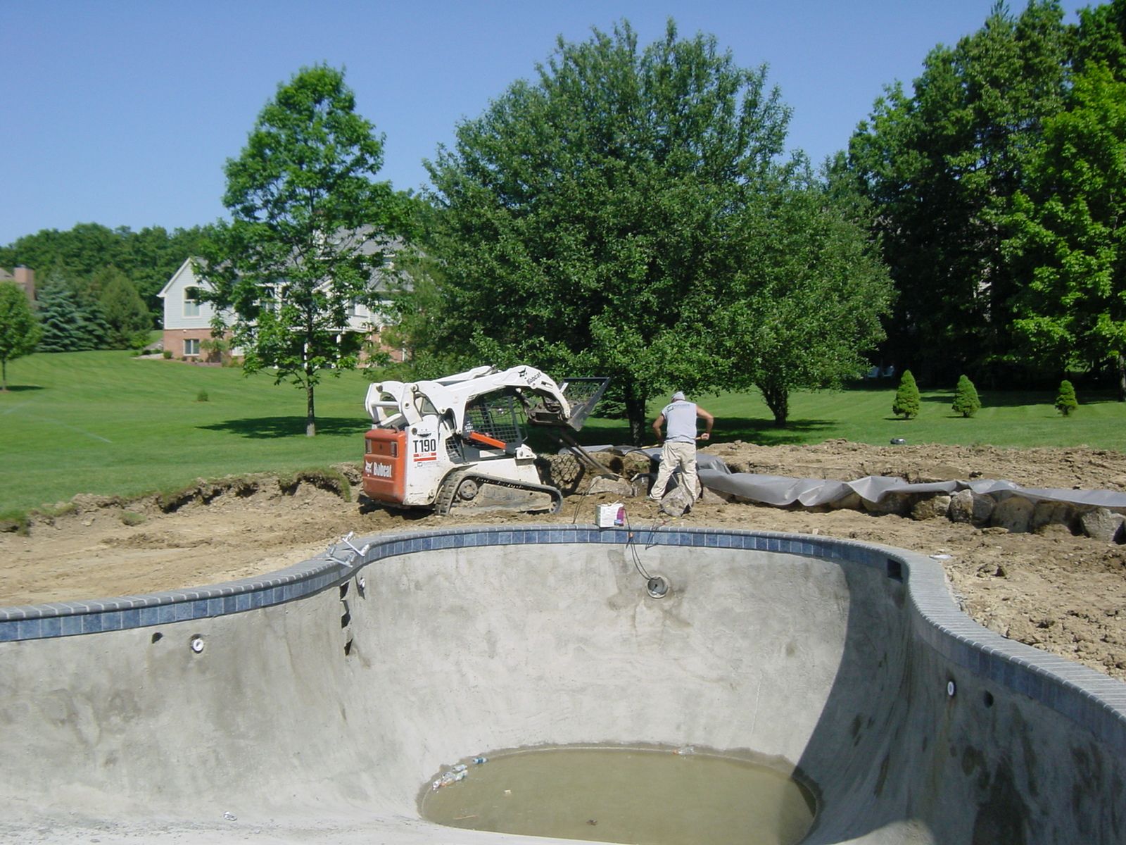 Pool construction site with a Bobcat, a worker, and a partially built pool.