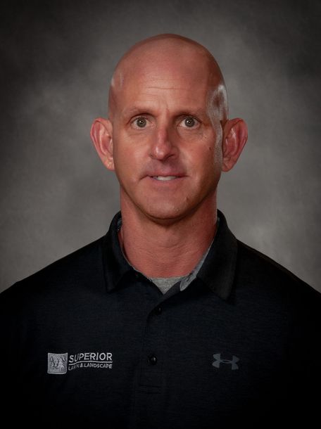 Bald man in black shirt, slightly smiling, headshot, gray background.