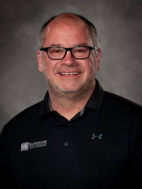 Man wearing glasses, black shirt, smiling; office background.