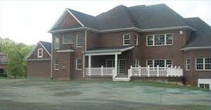 Two-story brick house with dark roof and white trim. Features a porch and multiple windows.
