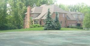 Brick house with a brown roof and a green lawn, set among tall trees.