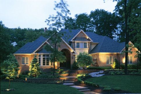Lit-up brick house with a blue roof and landscaped front yard at dusk.