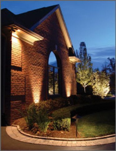 Night view of a brick house with outdoor lighting illuminating the facade and landscaping.