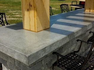 Outdoor bar with a concrete countertop, wood post, and black wrought-iron chairs.