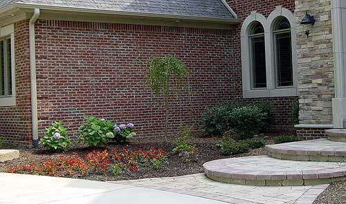 Red brick house exterior with landscaped garden bed and stone pathway.