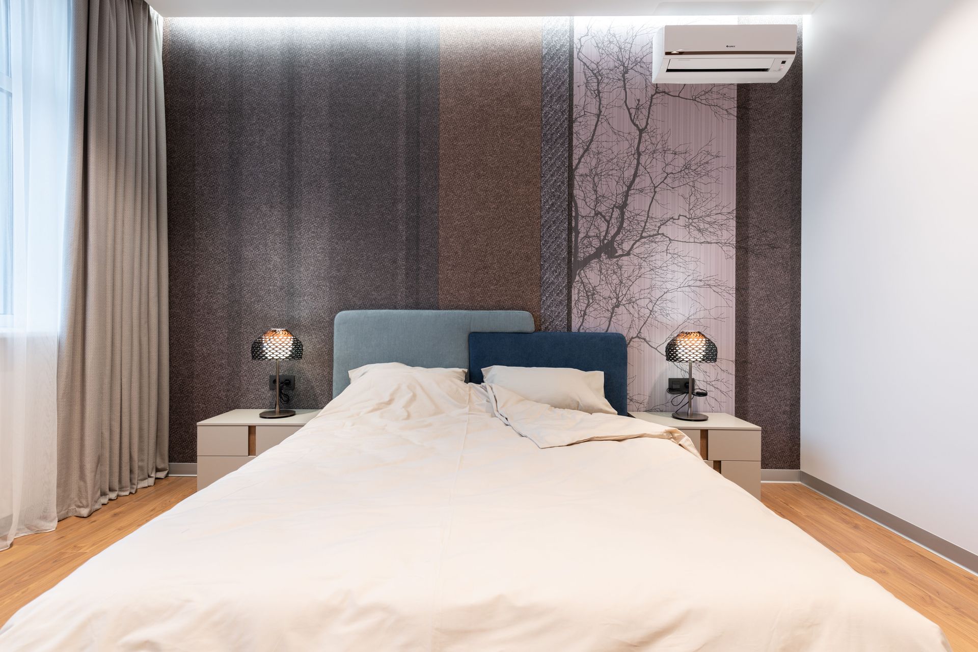 Modern bedroom with a large bed, blue headboard, bedside lamps, curtains, and patterned accent wall.