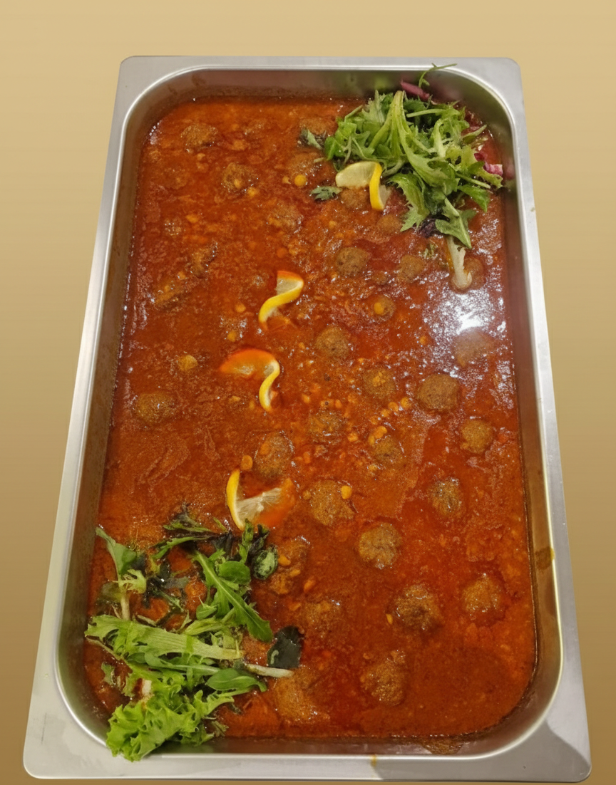Köttbullar i tomatsås i en metallbricka, garnerade med grönsaker och citronskivor.