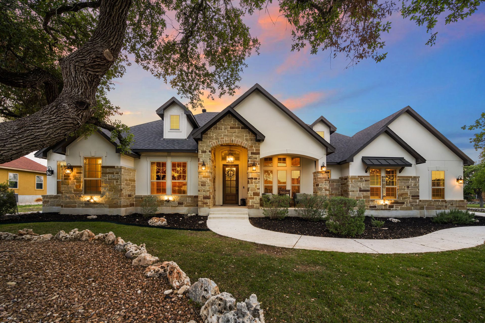 Luxurious suburban house at dusk with warm lights, arched entry, and landscaped front yard