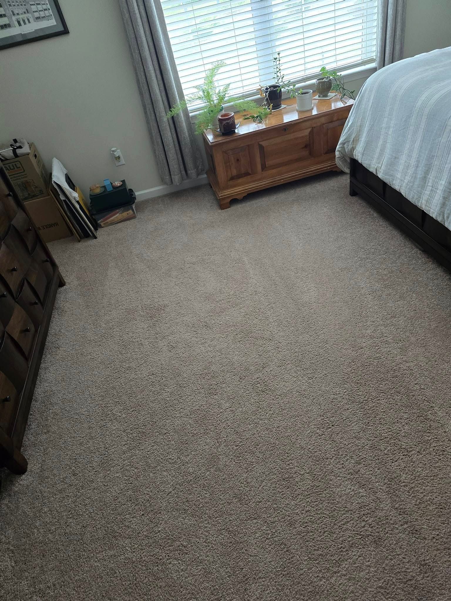 Carpeted bedroom with a bed, window curtains, and a small wooden table by the window.