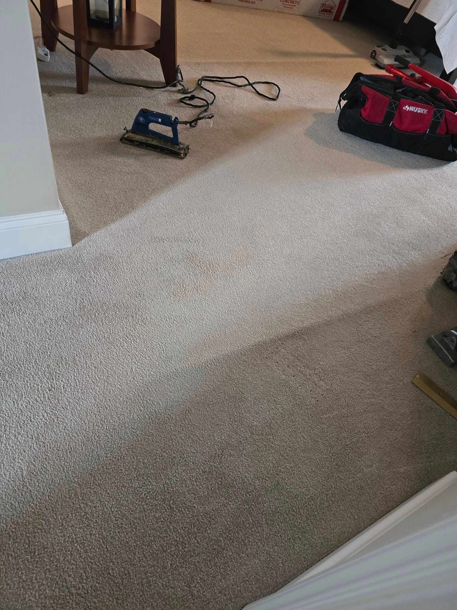 Carpeted living room floor with a small black device and a red tool bag near a wall.