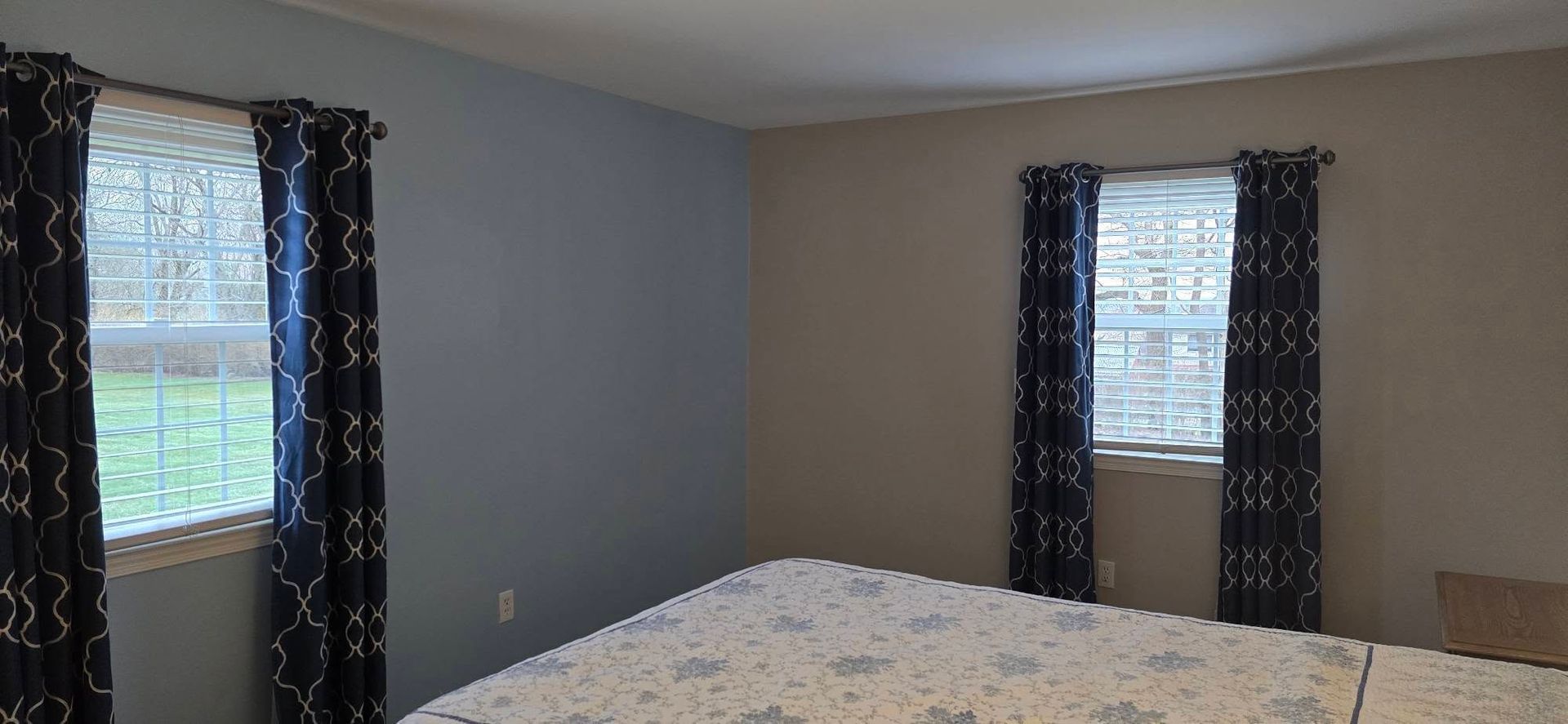 Bedroom with gray walls, bed, and two windows with dark curtains and blinds