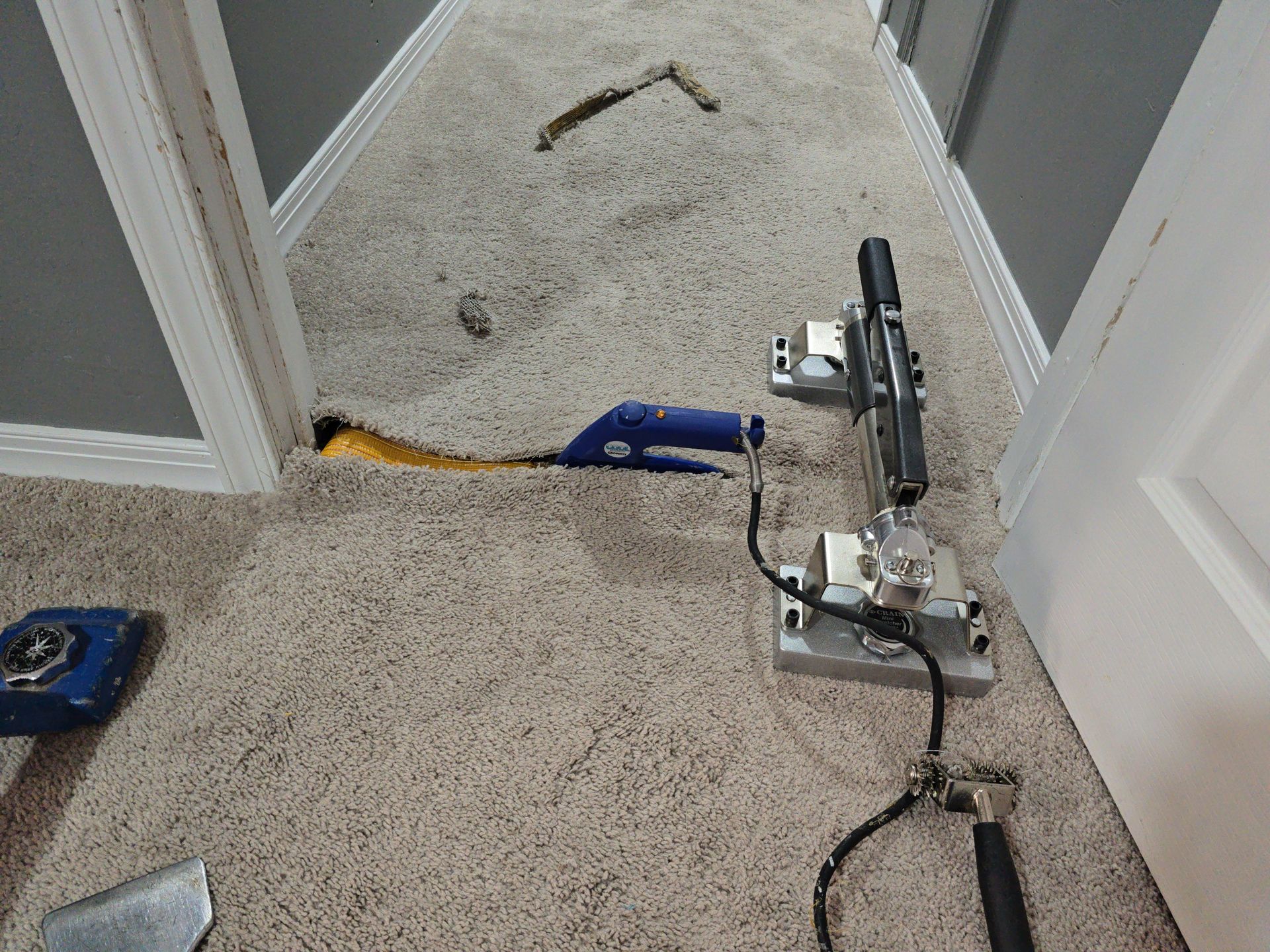 Carpeted hallway with a floor-cleaning machine and power cord, plus a blue tool on the floor