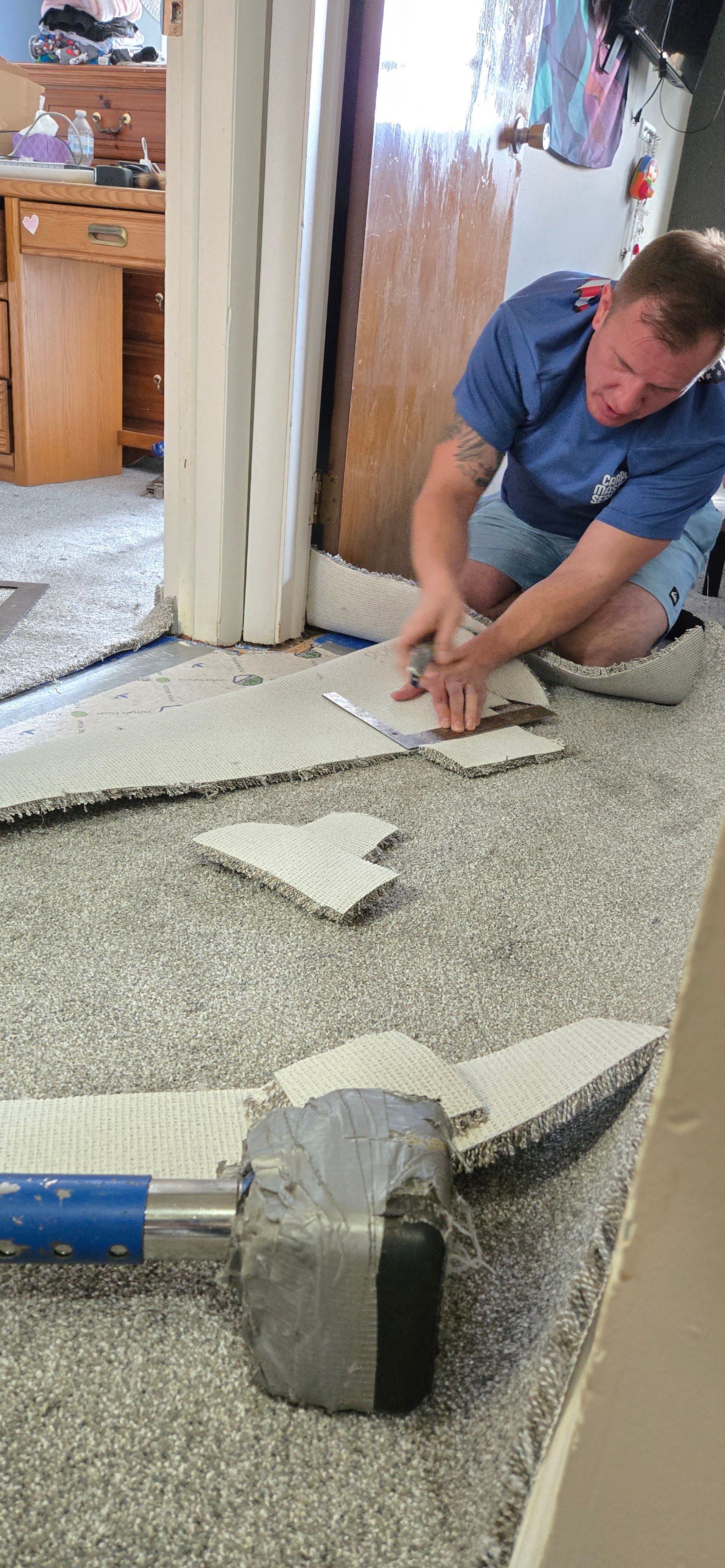 Worker kneeling on carpet, cutting floor tile with a hand tool during home renovation
