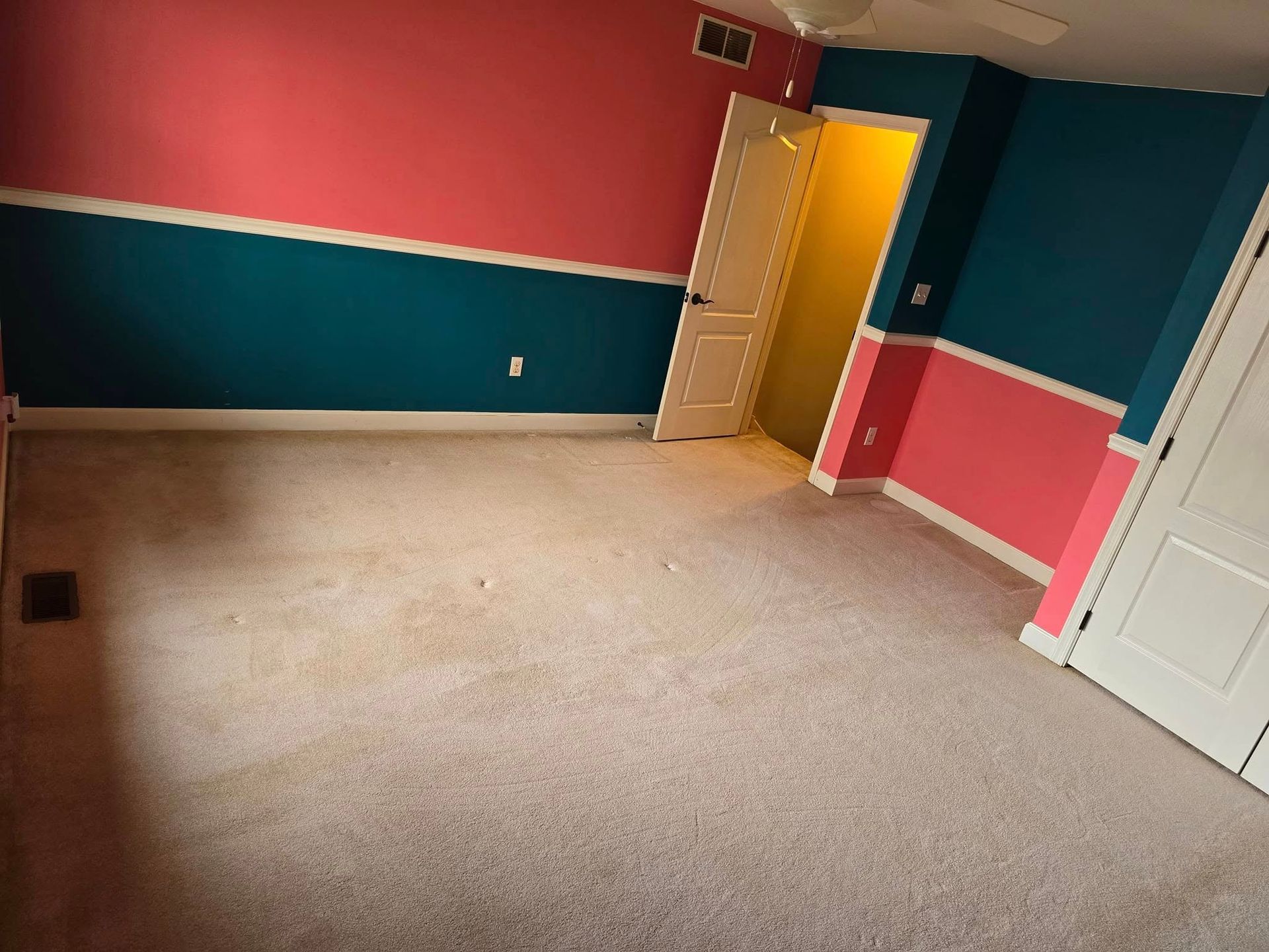 Empty room with pink, teal, and cream walls, beige carpet, and a white door.