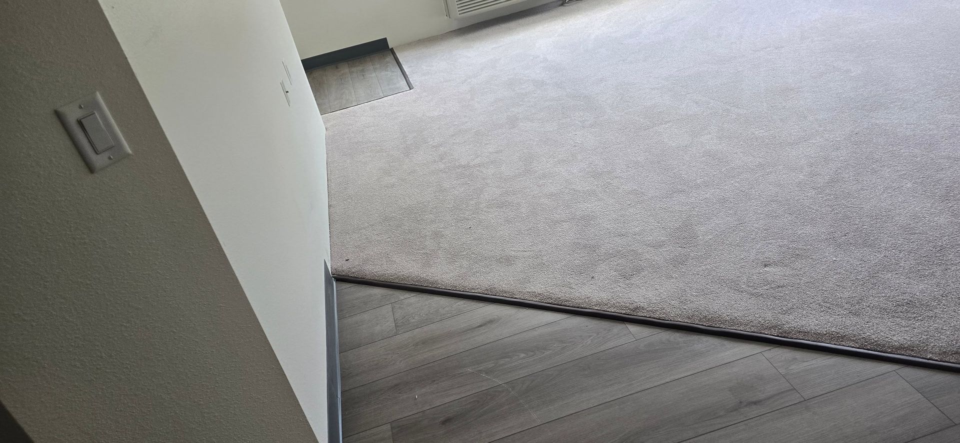 Empty room corner with gray carpet and dark wood flooring