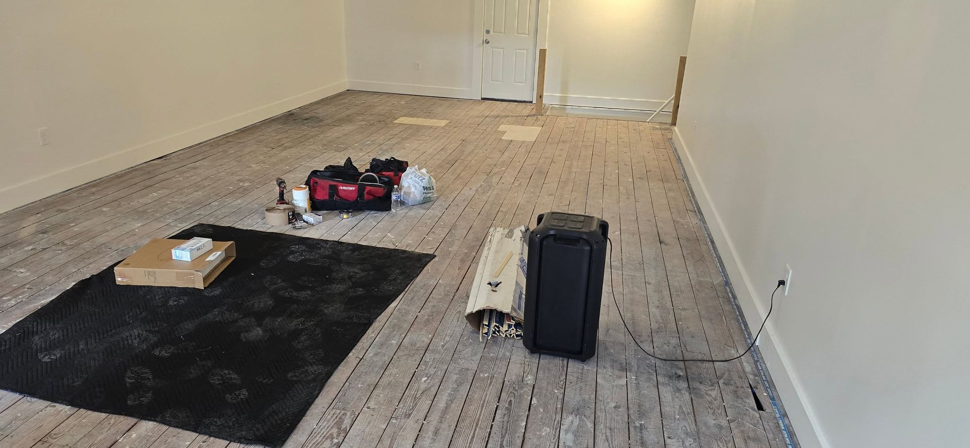 Empty carpeted room with a few items on the floor and a black suitcase near the center