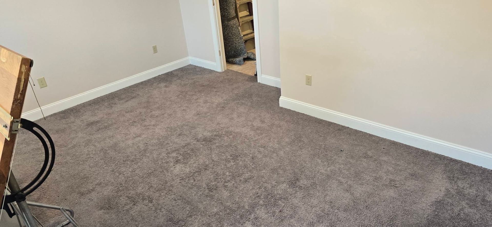 Empty carpeted room with beige walls and a doorway to an unfinished area