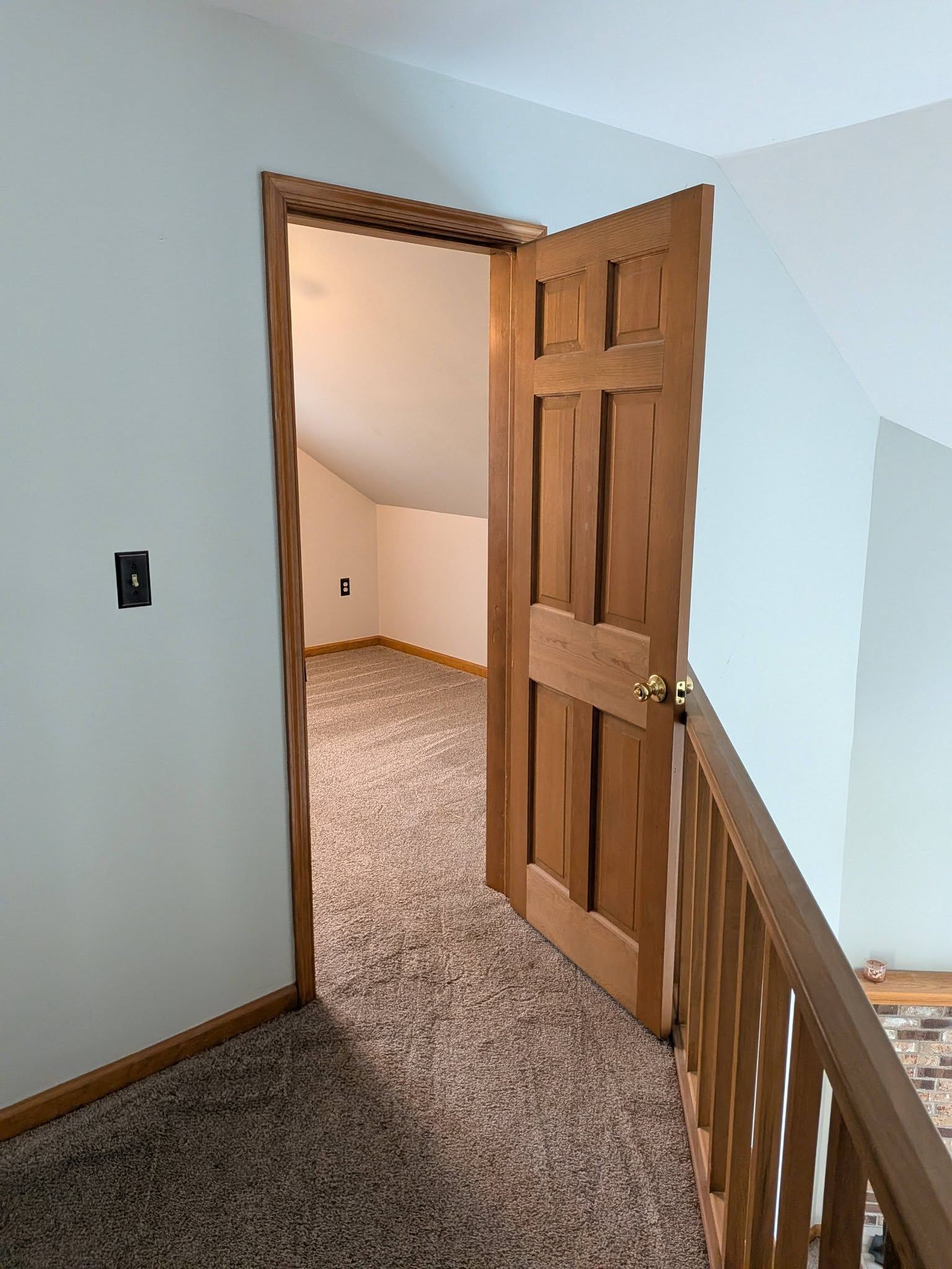 Wooden door open into a carpeted upstairs hallway with light blue walls and wood trim.