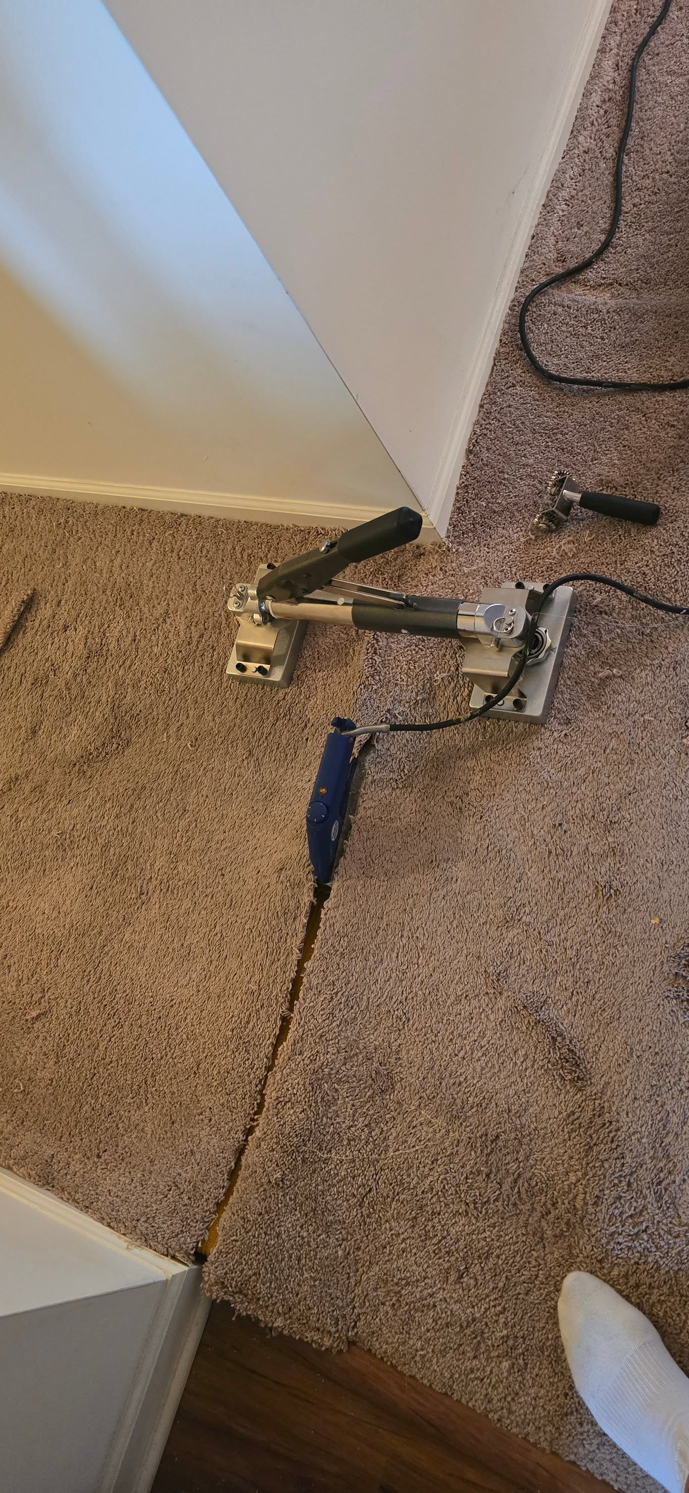 Broken items scattered on carpet beside a wall and cord, with a blue-handled tool nearby