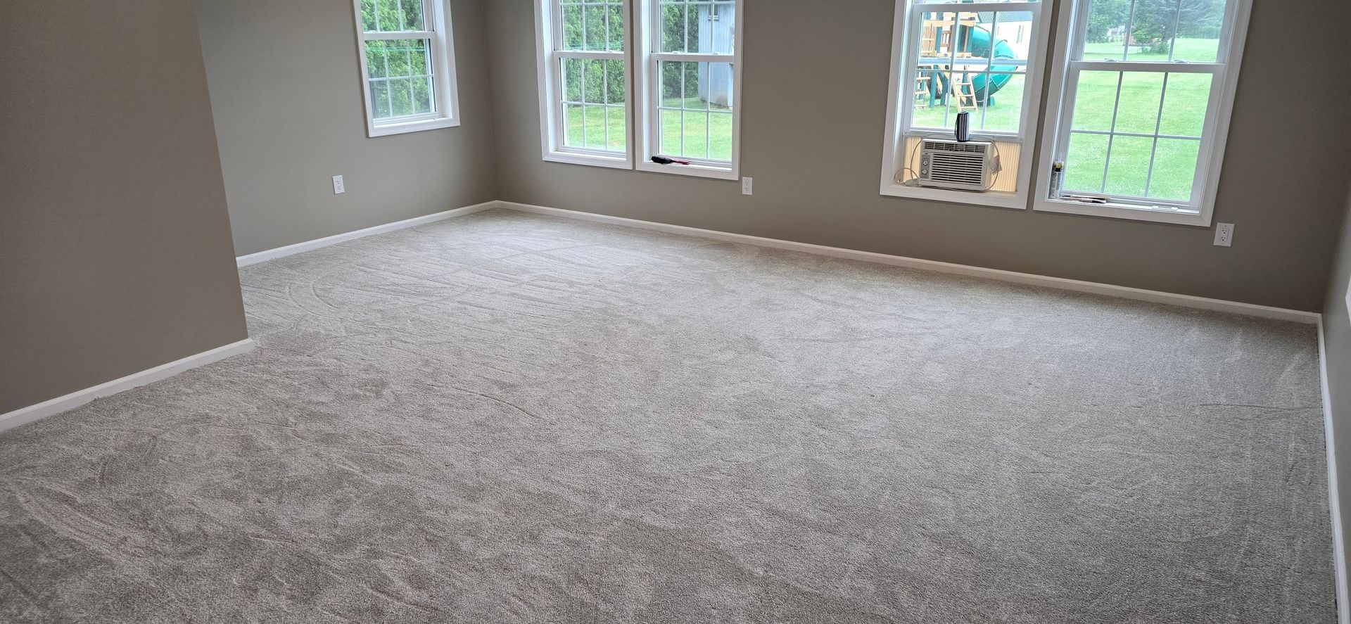 Empty carpeted living room with large windows and natural light