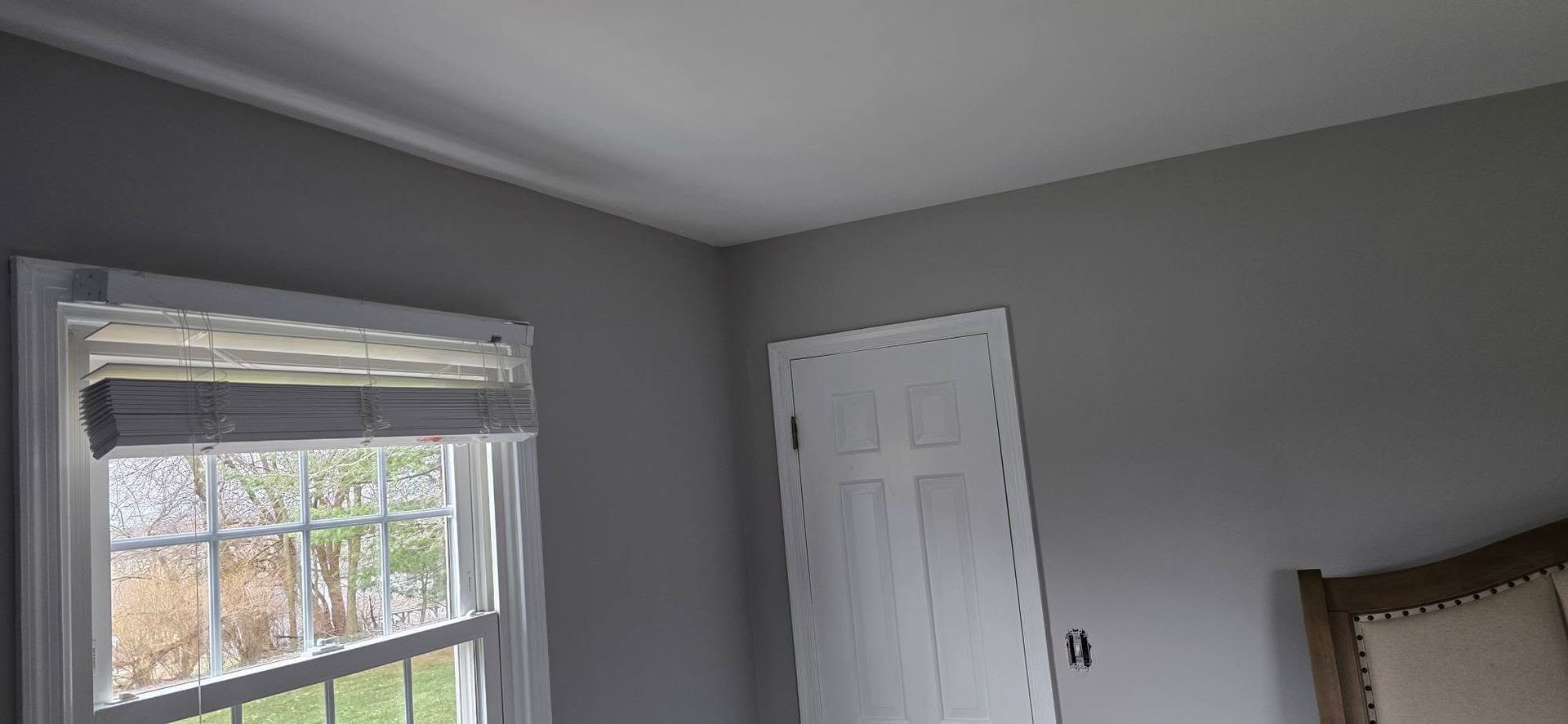 Gray bedroom corner with a window, white closet doors, and part of a bed visible